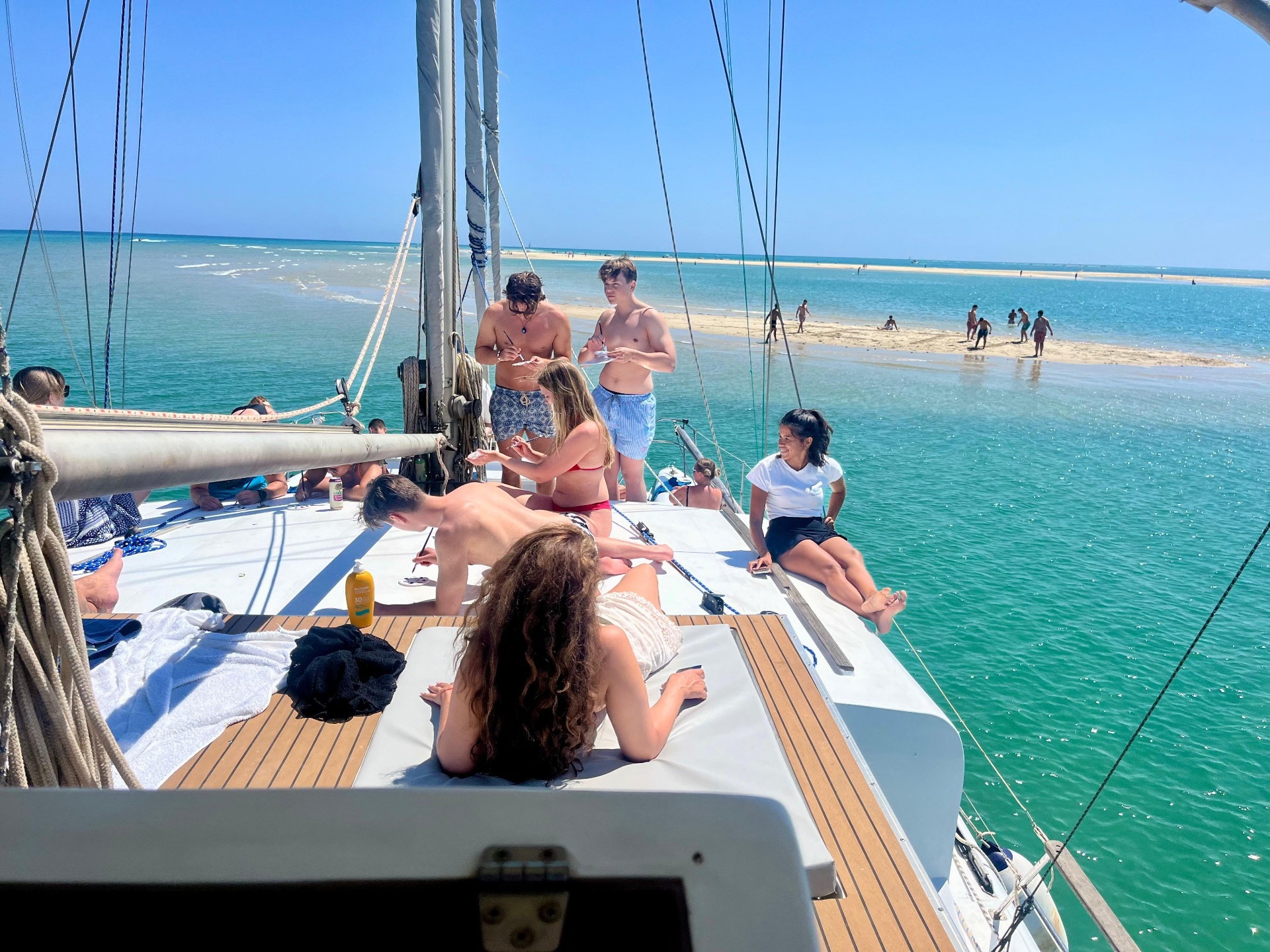 Guests relaxing on the catamaran deck beside a turquoise sandbank